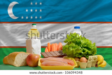 complete national flag of uzbekistan covers whole frame, waved, crunched and very natural looking. In front plan are fundamental food ingredients for consumers, symbolizing consumerism an human needs