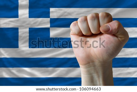 complete national flag of greece covers whole frame, waved, crunched and very natural looking. In front plan is clenched fist symbolizing determination