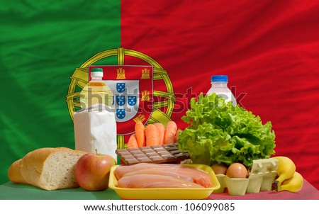 complete national flag of portugal covers whole frame, waved, crunched and very natural looking. In front plan are fundamental food ingredients for consumers, symbolizing consumerism