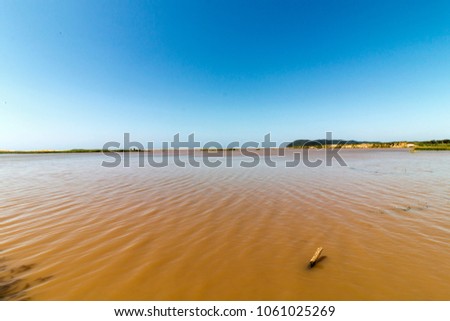  Rippled brown muddy water, green vegetation and blue sky landscape at St Lucia Estuary in iSimangaliso Wetland Park in Zululand, South Africa