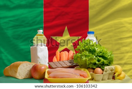 complete national flag of cameroon covers whole frame, waved, crunched and very natural looking. In front plan are fundamental food ingredients for consumers, symbolizing consumerism an human needs