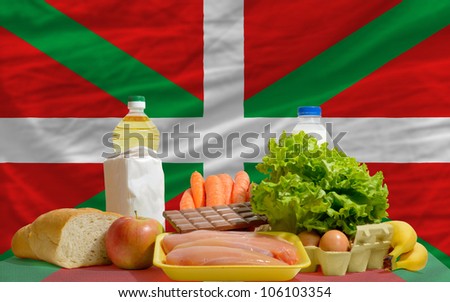 complete national flag of basque covers whole frame, waved, crunched and very natural looking. In front plan are fundamental food ingredients for consumers, symbolizing consumerism an human needs