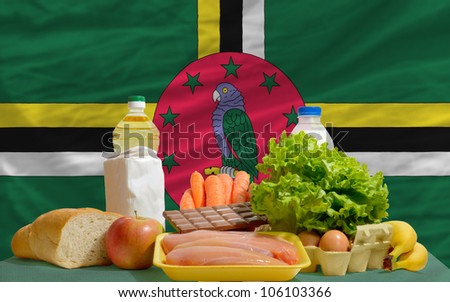 complete national flag of dominica covers whole frame, waved, crunched and very natural looking. In front plan are fundamental food ingredients for consumers, symbolizing consumerism an human needs