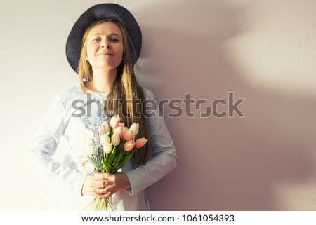 A young beautiful girl with blond dissolved long hair, a felt hat on her head, keeps spring flowers in her hands on a sunny day. Women's Day.