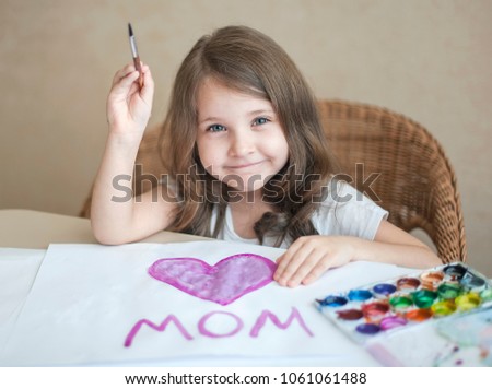 Child making homemade greeting card. A little girl paints a heart  on a homemade greeting card as a gift for Mother Day. Traditional play concept. Arts and crafts concept