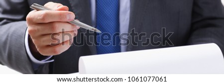 Male arm in suit and tie fill form clipped to pad with silver pen closeup. Sign gesture read pact sale agent bank job make note loan credit mortgage investment finance chief legal law concept