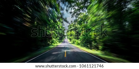 Empty asphalt road and speed motion blur on highway in summer with green tree forest at countryside. Road trip travel. Drive fast on the asphalt road in the forest. Summer vacation at tropical forest.