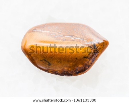 macro shooting of natural mineral rock specimen - tumbled tiger's eye gemstone on white marble background from South Africa