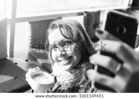 Portrait of a beautiful brunette taking a selfie with her smart phone at cafe. Black and white photo