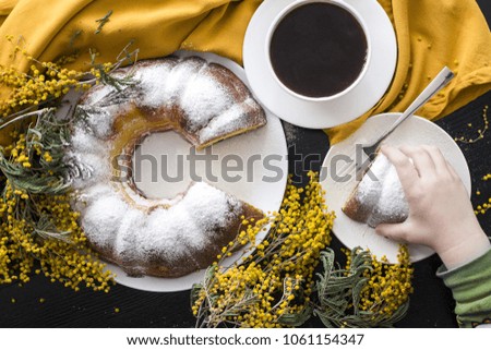 
Appetizing curd cake with a cup of coffee, a plate and a fork decorated with a mimosa flower and an orange tissue napkin