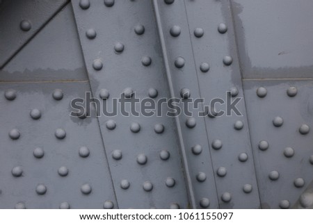 Close up outdoor view of a french metallic bridge detail. Beams, sheets and painted rivets visible. Grey iron surface. Abstract architectural image. Composition with points and lines in perspective. 