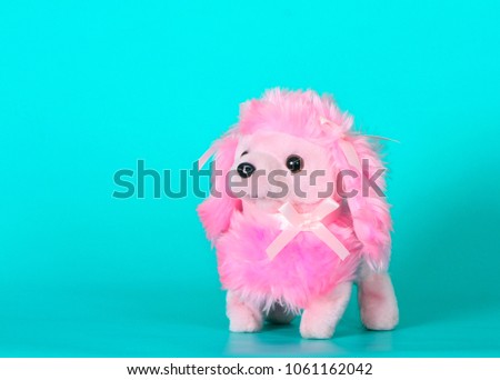 Pink toy dog on turquoise background. Cute plush animal with a bow. Horizontal image. Free space for text.