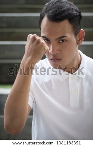 strong man clenching his fist portrait; man fighter in fist fighting pose looking at you; asian young adult man model