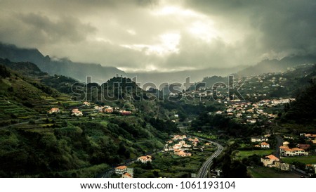 Aerial view on small city Sao Vicente - red rooftops, chapel on the hill, huge mountains on background and beautiful soft sunlight, Madeira island, Portugal.