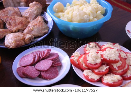 Pictured in the photo dishes of tomato, sausage, meat and potatoes on the table.