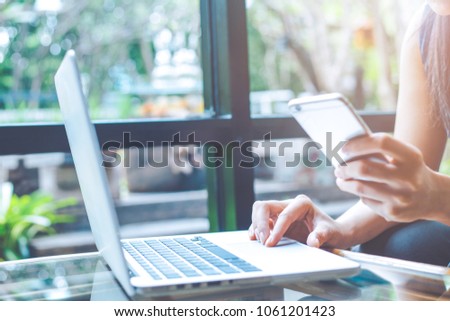 Business woman hand using a cell phone and working with a laptop computer  in the office.