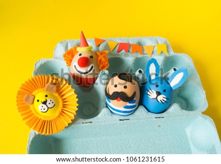 The concept of Easter with cute and cheerful handmade eggs, a rabbit, a clown, a strongman and a lion.Circus Yellow background. Funny egg. Painted Easter eggs in different moods and facial expression 