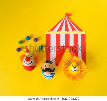 The concept of Easter with cute and cheerful handmade eggs, a clown, a strongman and a lion.Circus Yellow background. Funny egg. Painted Easter eggs in different moods and facial expression 