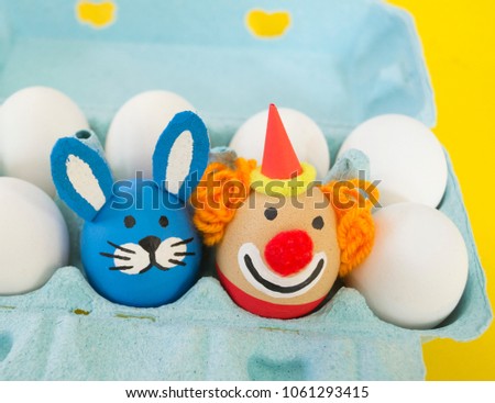 The concept of Easter with cute and cheerful handmade eggs, a rabbit, a clown.Circus Yellow background. Funny egg. Painted Easter eggs in different moods and facial expression 