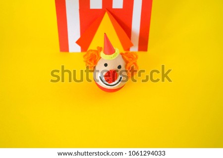 The concept of Easter with cute and cheerful handmade eggs, a clown.Circus Yellow background. Funny egg. Painted Easter eggs in different moods and facial expression 