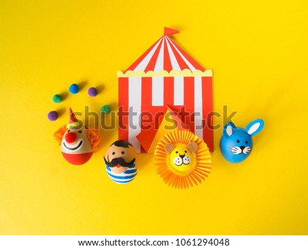 The concept of Easter with cute and cheerful handmade eggs, a rabbit, a clown, a strongman and a lion.Circus Yellow background. Funny egg. Painted Easter eggs in different moods and facial expression 
