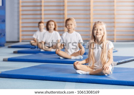 Smiling girl sitting on a blue mat during gymnastics classes