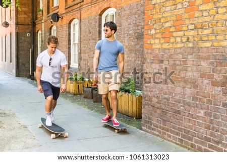 Two men going by skateboard on the pavement in London. Friends having fun together on a summer day in the city. Lifestyle and hobby concepts