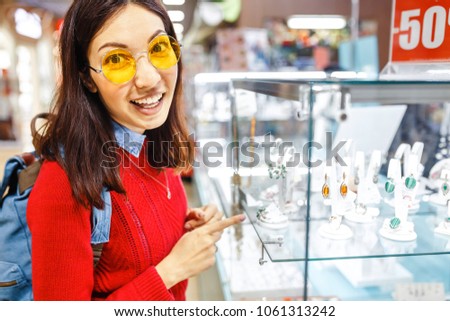 Asian hipster woman chooses jewelry in a store and looks at the display case