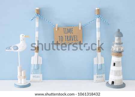 nautical concept with wooden decorative boat oars and hanging note message on a string next to lighthouse and seagull over blue background