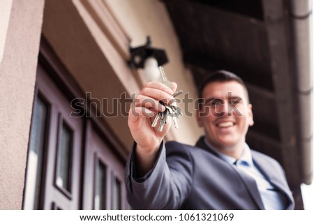 Male Realtor Standing Outside Residential Property Holding Keys.
