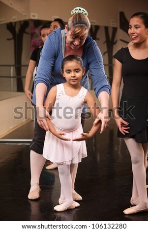 Ballet class instructor helps young student with fourth position