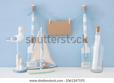 nautical concept with hanging empty note on a string next to boat, letter in the bottle and seagull over blue background