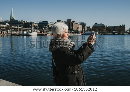 Sweet middle-aged woman with withe hair taking some pictures from her travel to Stockholm in Sweden from a beautiful view from the old city. Lifestyle photography.