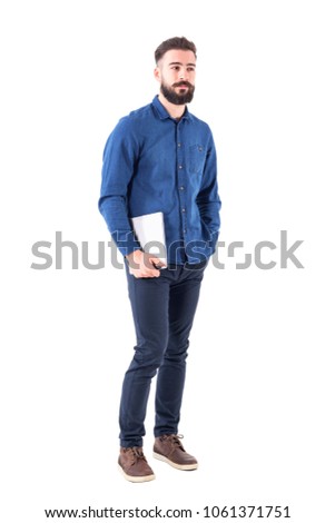 Relaxed young successful business employer holding tablet pad computer under the arm looking away. Full body isolated on white background.