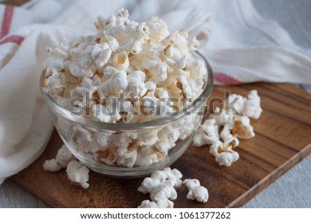 Popcorn in a glass cup on a wooden tray.