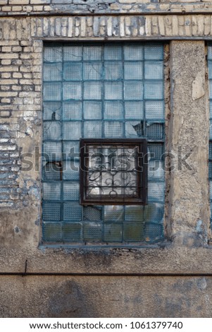The old window with glass blocks and rusty bars on a collapsing brick wall