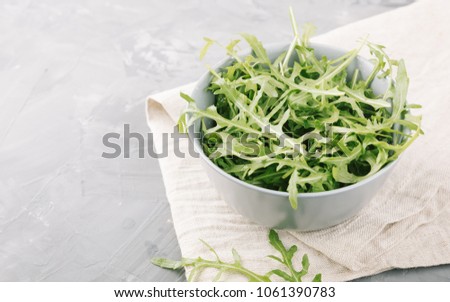 Fresh green arugula on a stone background. Garden rocket salad in a bowl on a grey table.