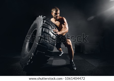 Muscular fitness shirtless man moving large tire in gym center, concept lifting, workout cross fit training Royalty-Free Stock Photo #1061404472