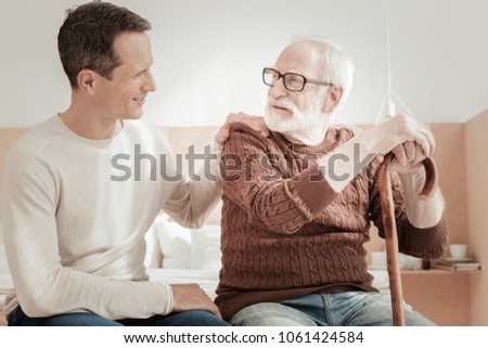 Best son. Satisfied unshaken aged man supporting on the cane smiling and looking at his son. Royalty-Free Stock Photo #1061424584