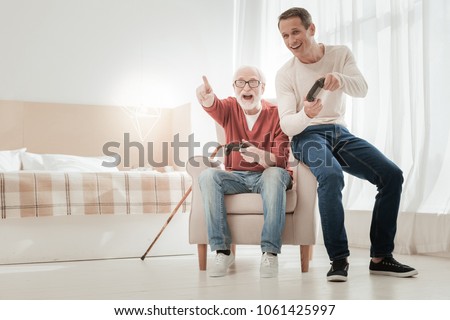 Did you see. Happy unshaken senior man sitting on the chair with a son pointing aside and laughing. Royalty-Free Stock Photo #1061425997
