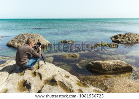 Man takes picture on the phone mounted on a tripod on a sea rocky coast