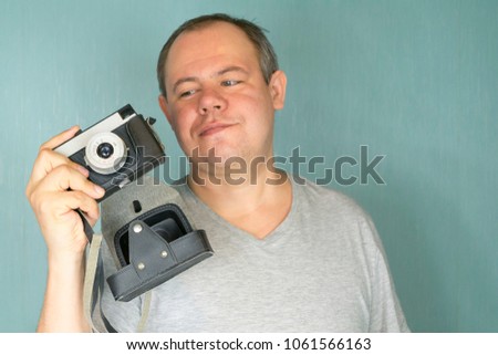 the guy holds in his hand an old film photo camera in a case with an open lens on a blue empty background