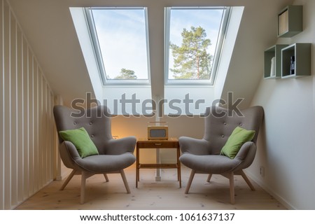 Modern retro design in a attic / loft. Small vintage table with a radio on and two reading chairs under two skylights. Roof / ceiling window.  Royalty-Free Stock Photo #1061637137