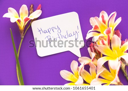 Note in shape of heart with words "Happy Birthday!" with flowers on purple surface.