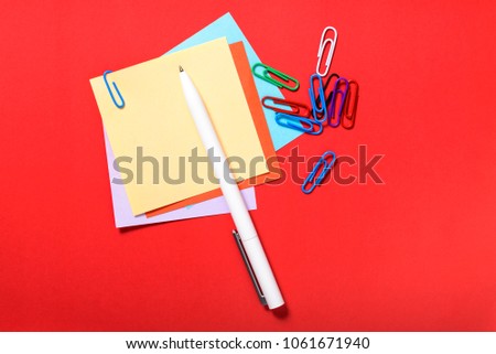 Multicolored stickers for notes, pen, paper clip on red background.