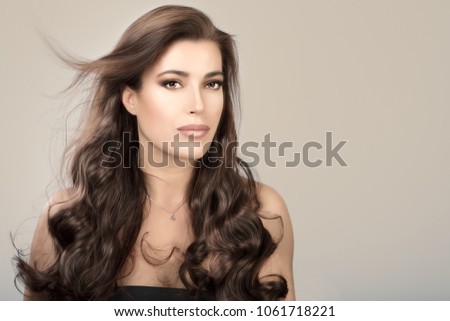 Beautiful model girl with healthy long wavy hair cascading over her shoulders over a beige studio background