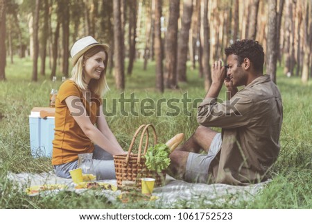 Cheese. Concentrated man taking photo of his girlfriend during picnic. Woman is sitting and smiling