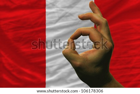 man showing excellence or ok gesture in front of complete wavy peru national flag symbolizing best quality, positivity and success
