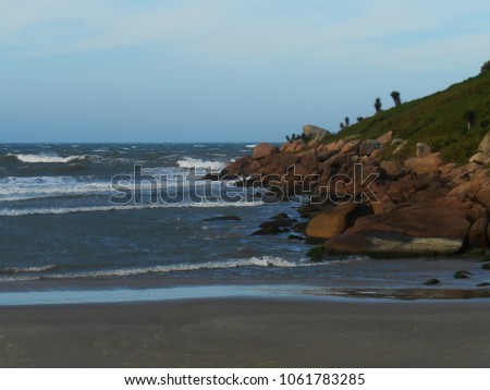dark sand and sea agitated by the wind and on the right side rocks of the Cape of Santa Marta, Laguna, SC, Brazil