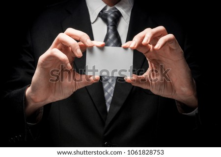 Close up of man in black suit holding business card on black background